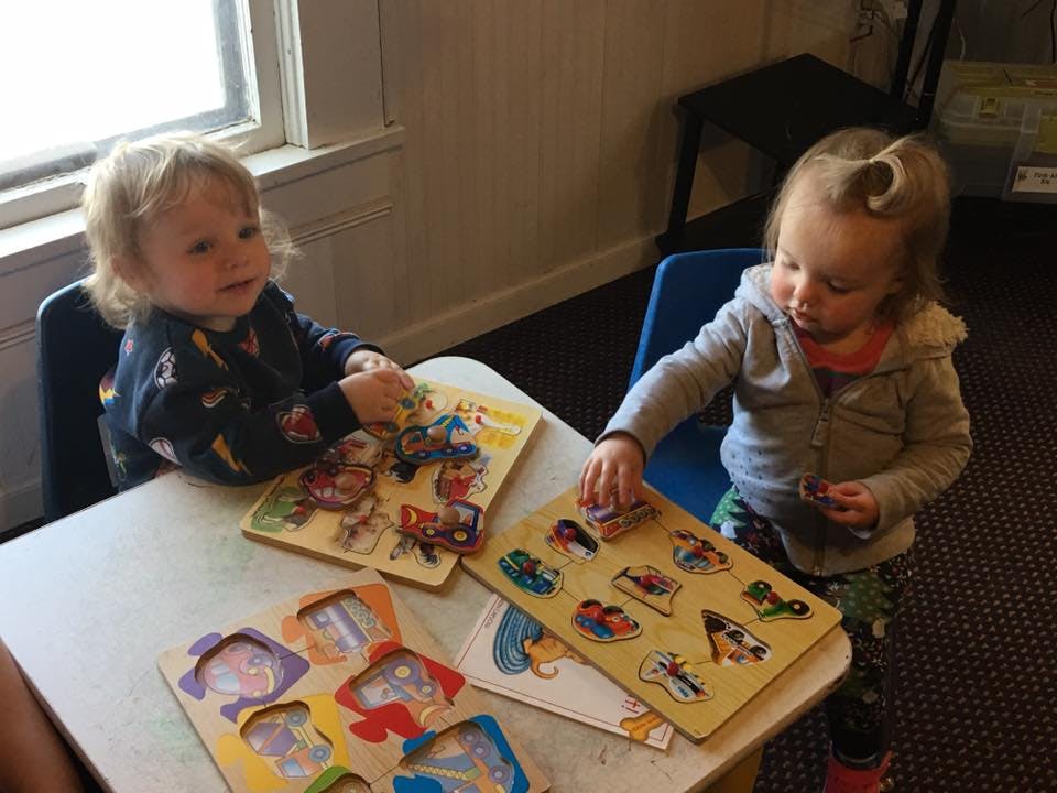 Two children playing with wooden puzzles at a table