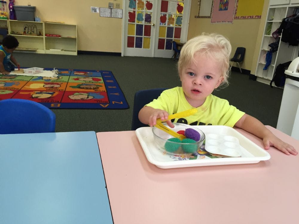 Child at a table with a tray of colorful items