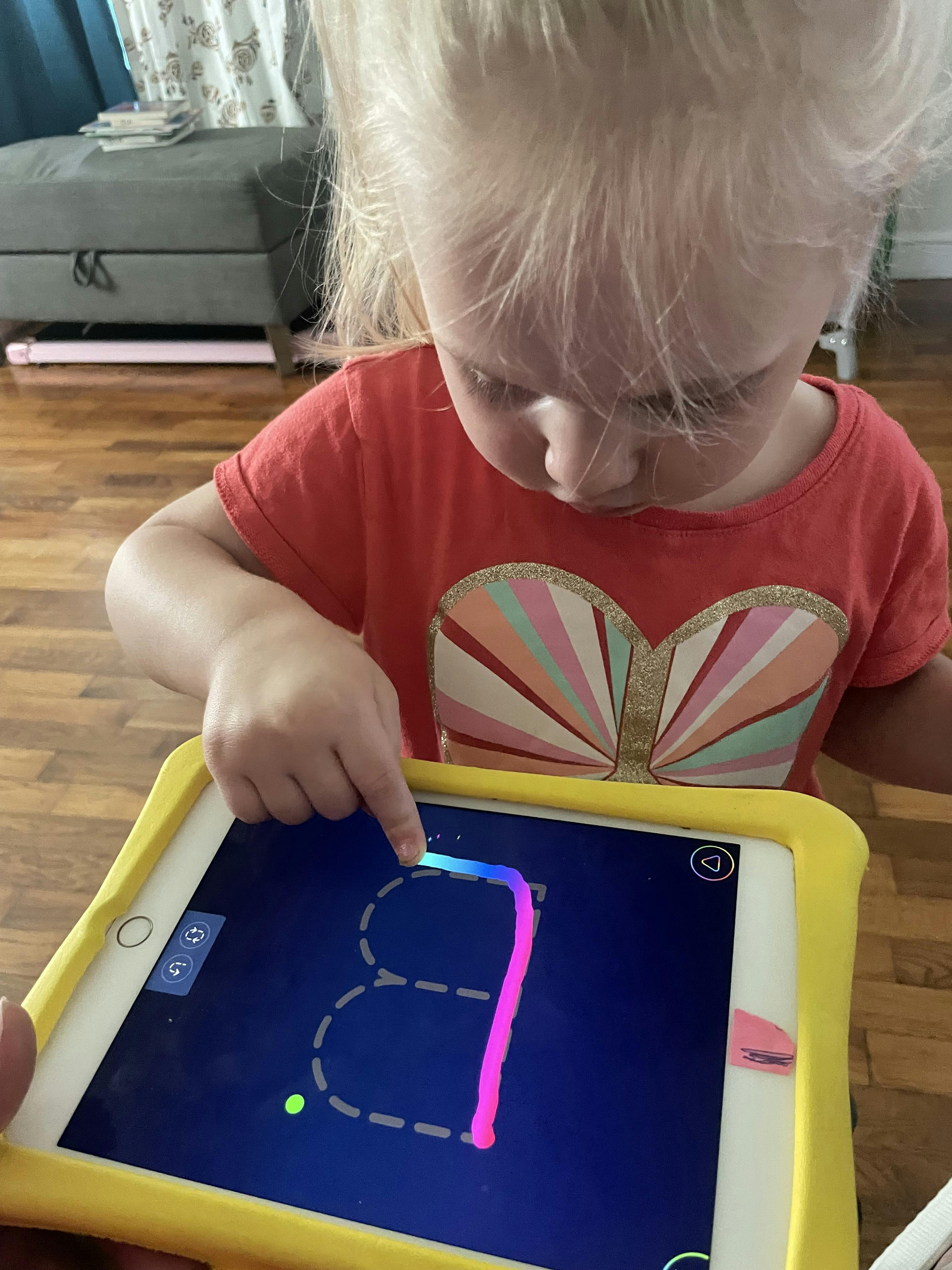 Child using a finger to trace a letter on a tablet screen