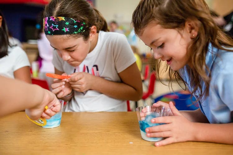 Two children at a table with cups, one holding a small orange object