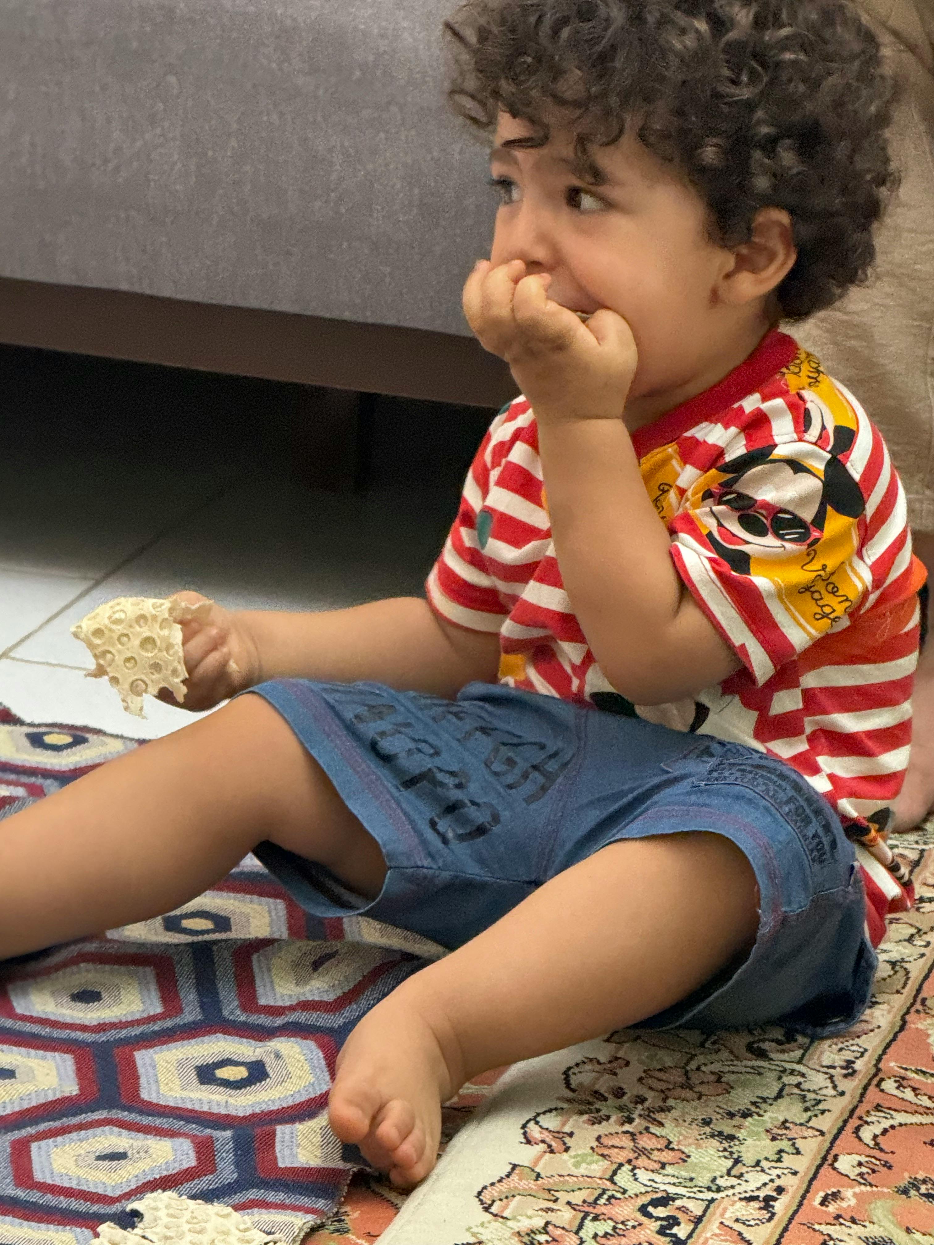 Child sitting on a rug, holding food and looking to the side