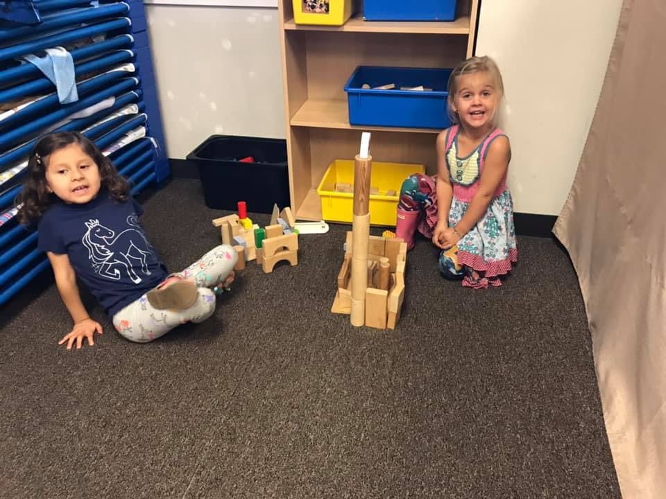 Two children playing with wooden blocks on a carpeted floor