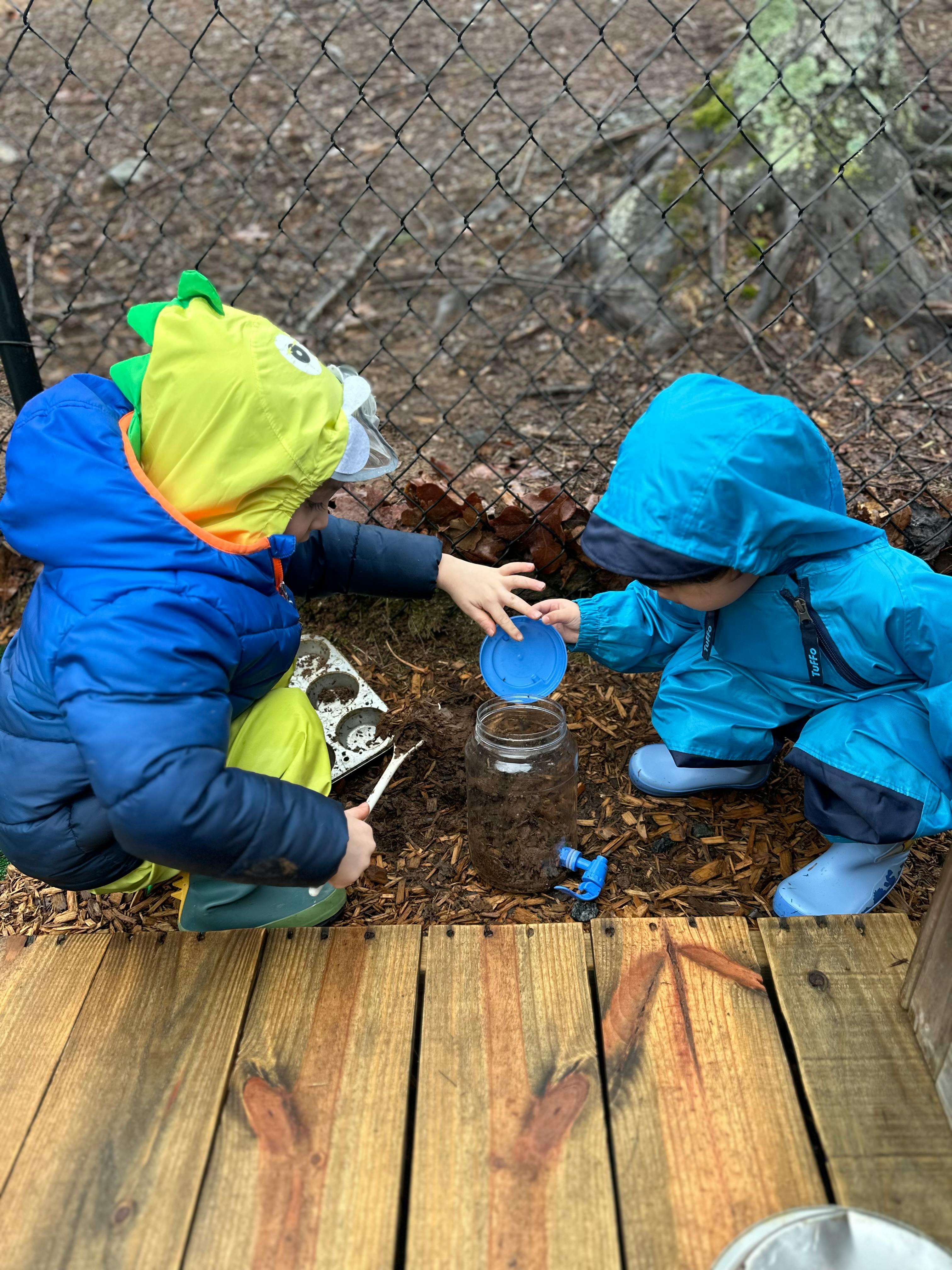 Two children playing with a jar and dirt outdoors