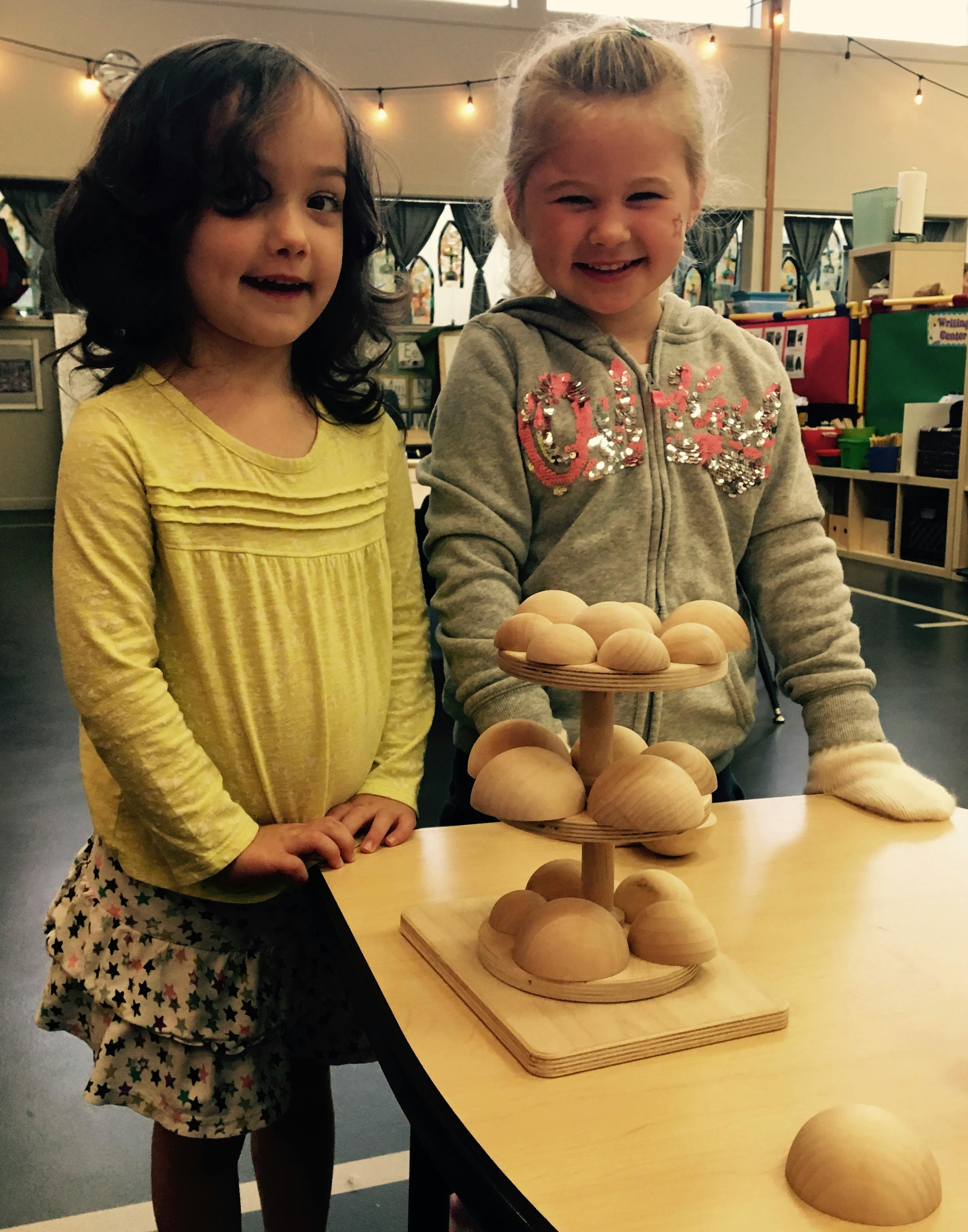 Two children standing next to a table with a wooden mushroom toy