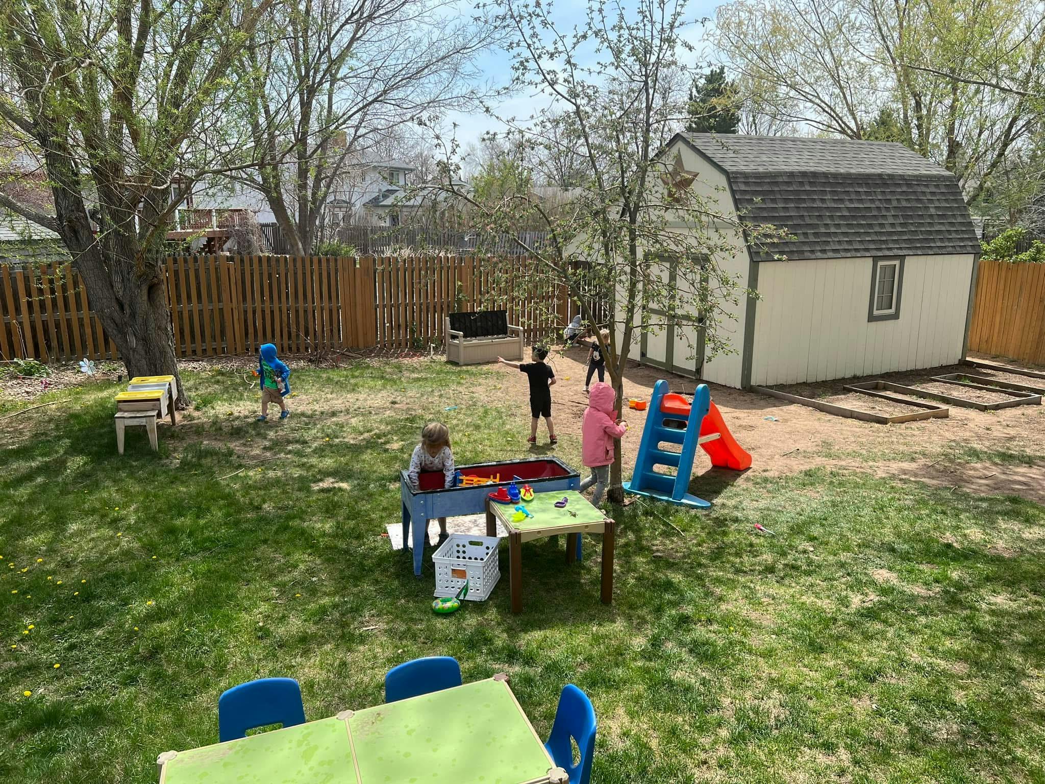 Children playing in a backyard with a shed, a sand and water table, and a slide