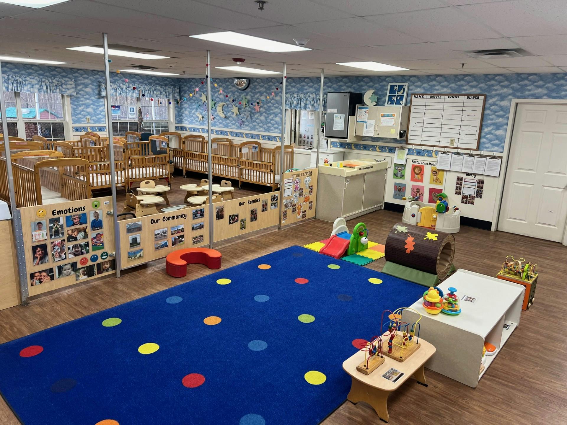 An empty daycare room with cribs, play area, and activity board