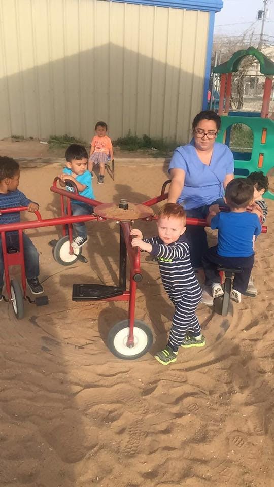 Adult and children playing on tricycles in a sandy area