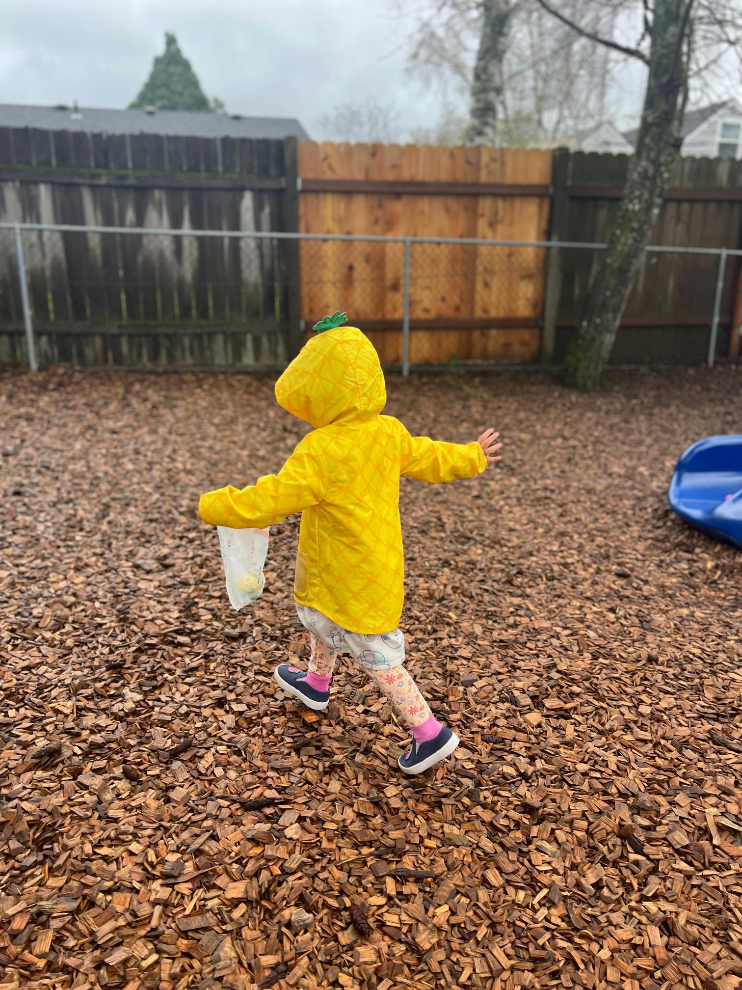 Child in yellow raincoat walking on wood chips