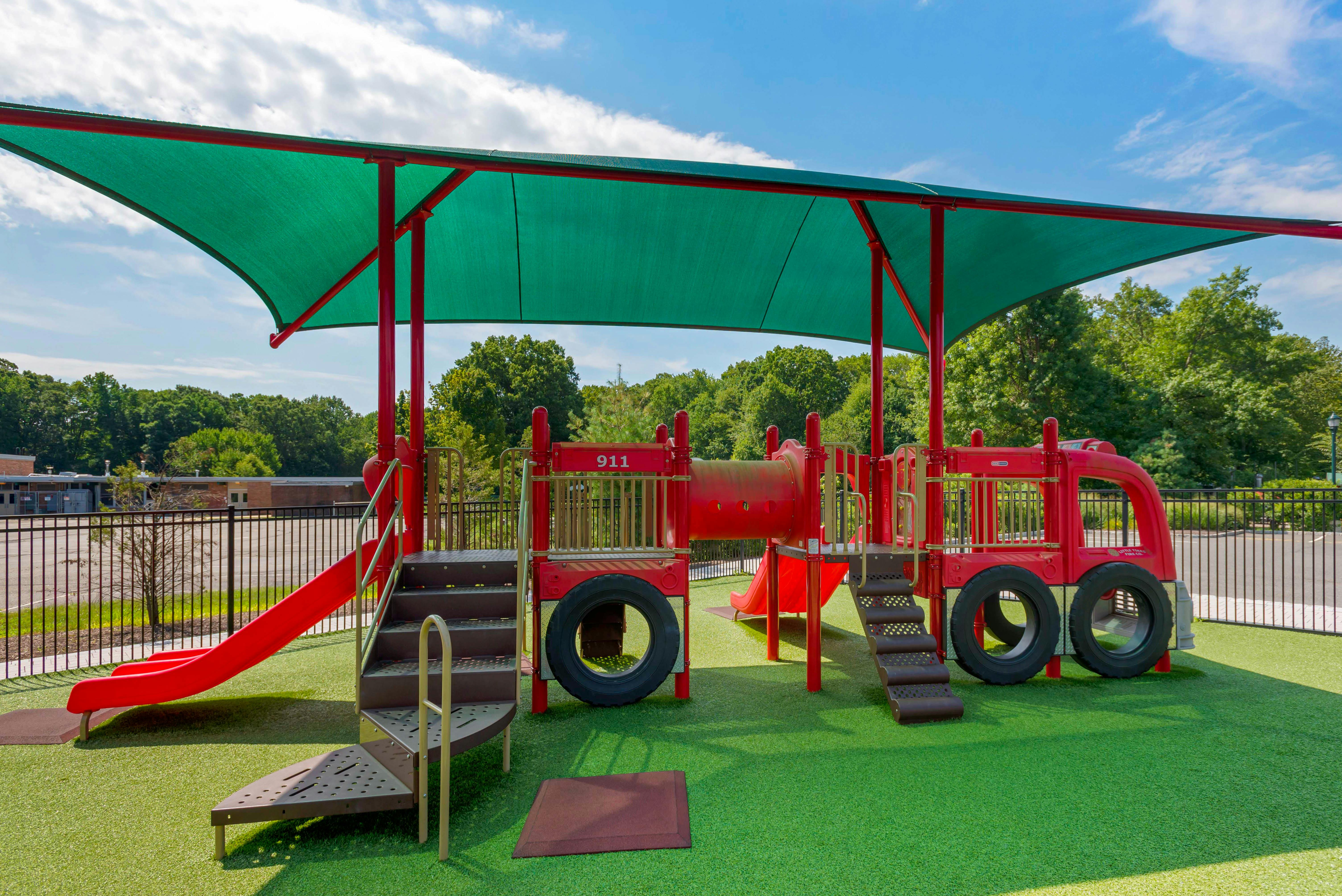 Red fire truck-themed playground equipment under a green shade canopy