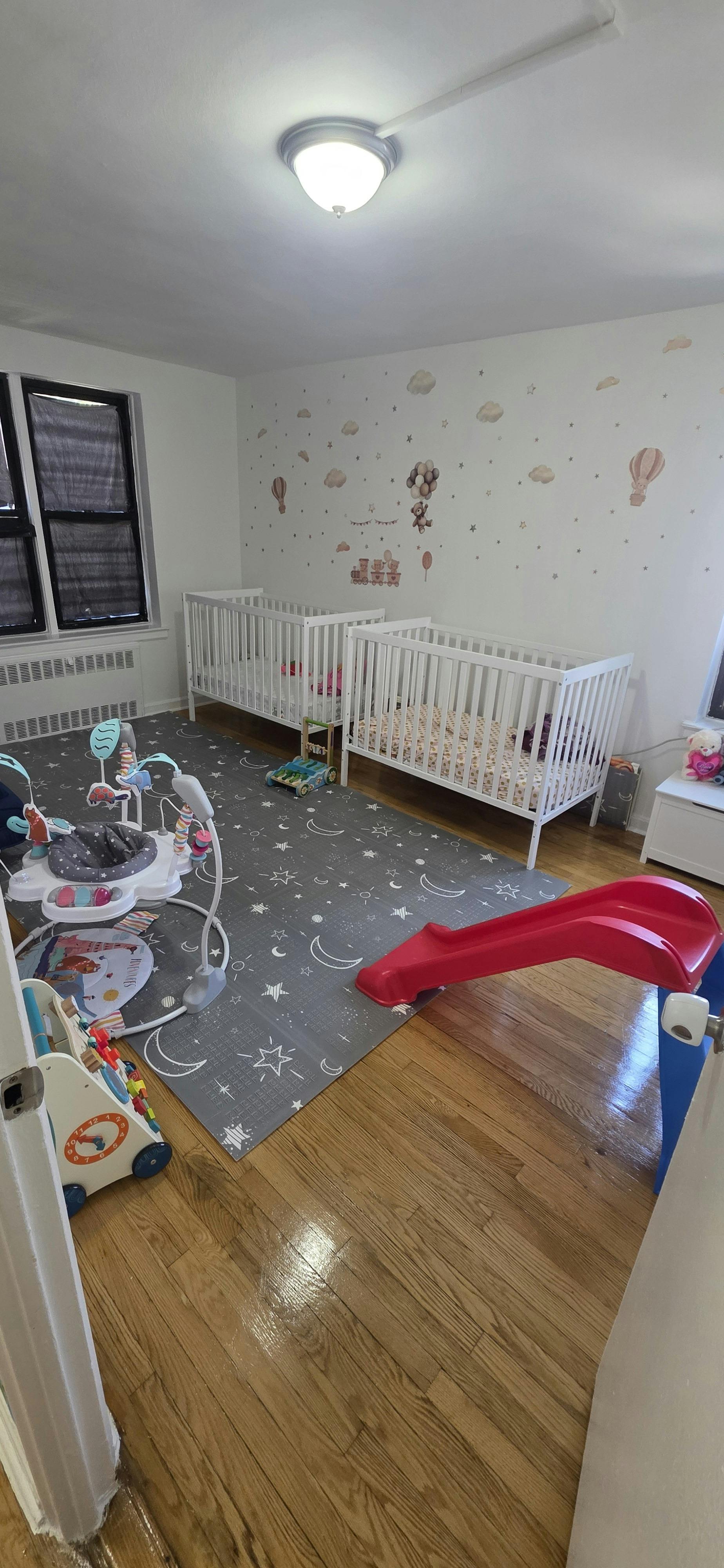 Two white cribs and play equipment in a nursery room