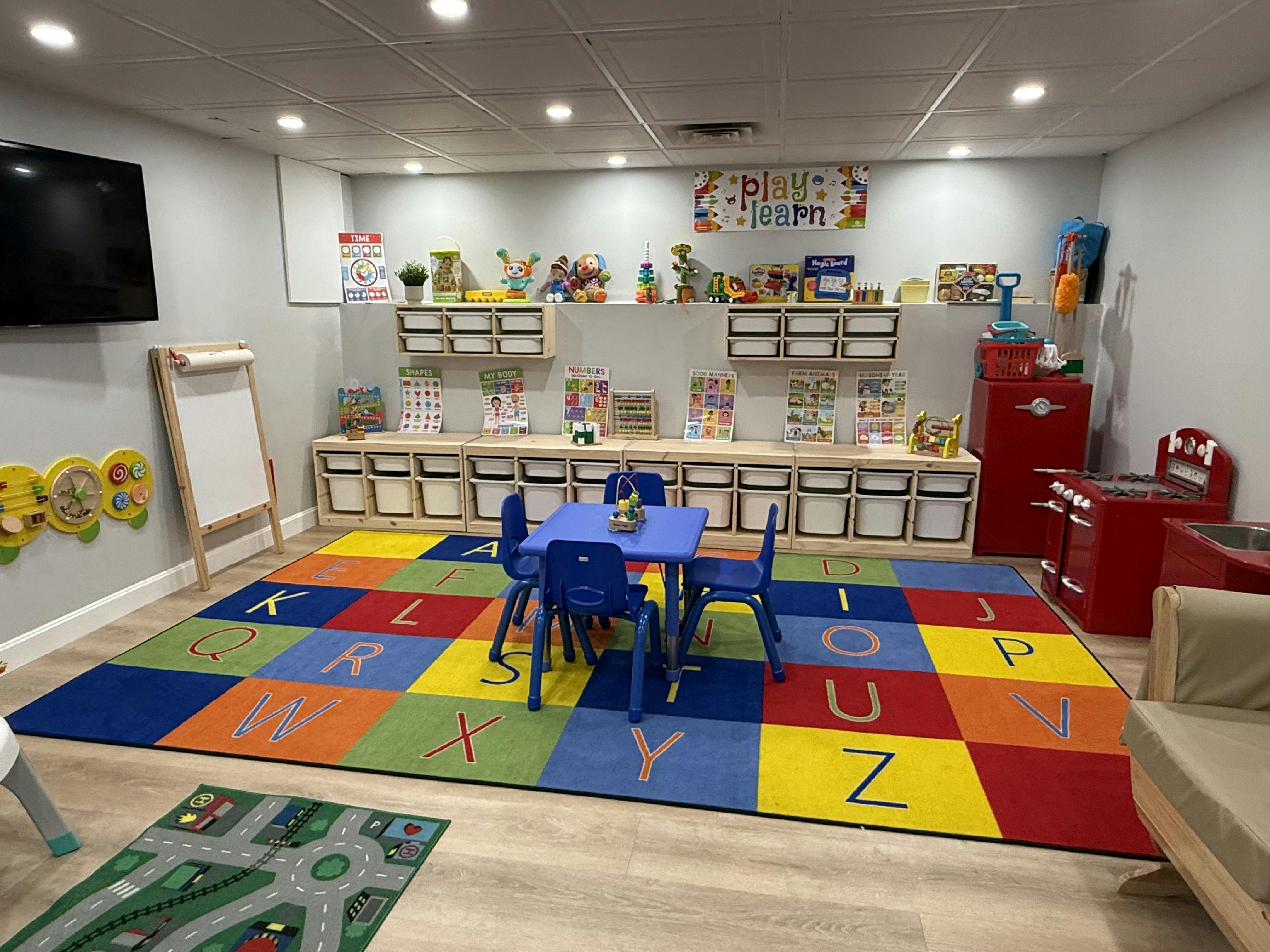 Playroom with a colorful alphabet rug, small table, and toys on shelving