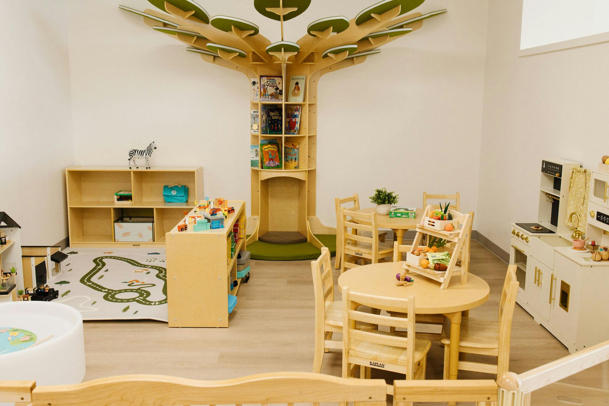 Playroom with wooden furniture including a tree-shaped bookshelf and toy kitchen