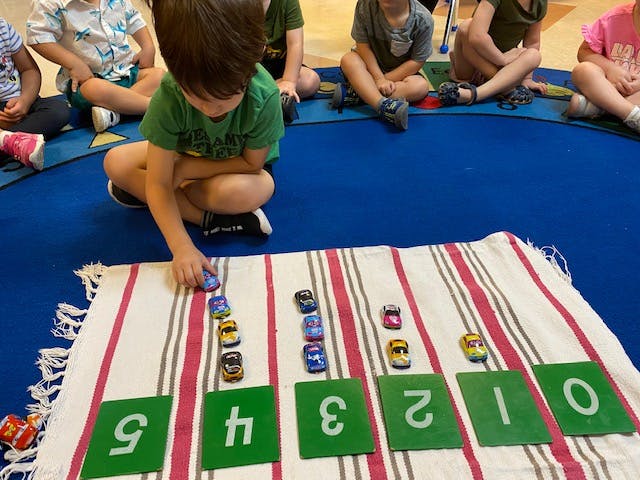 Child playing with toy cars and numbered cards in a classroom