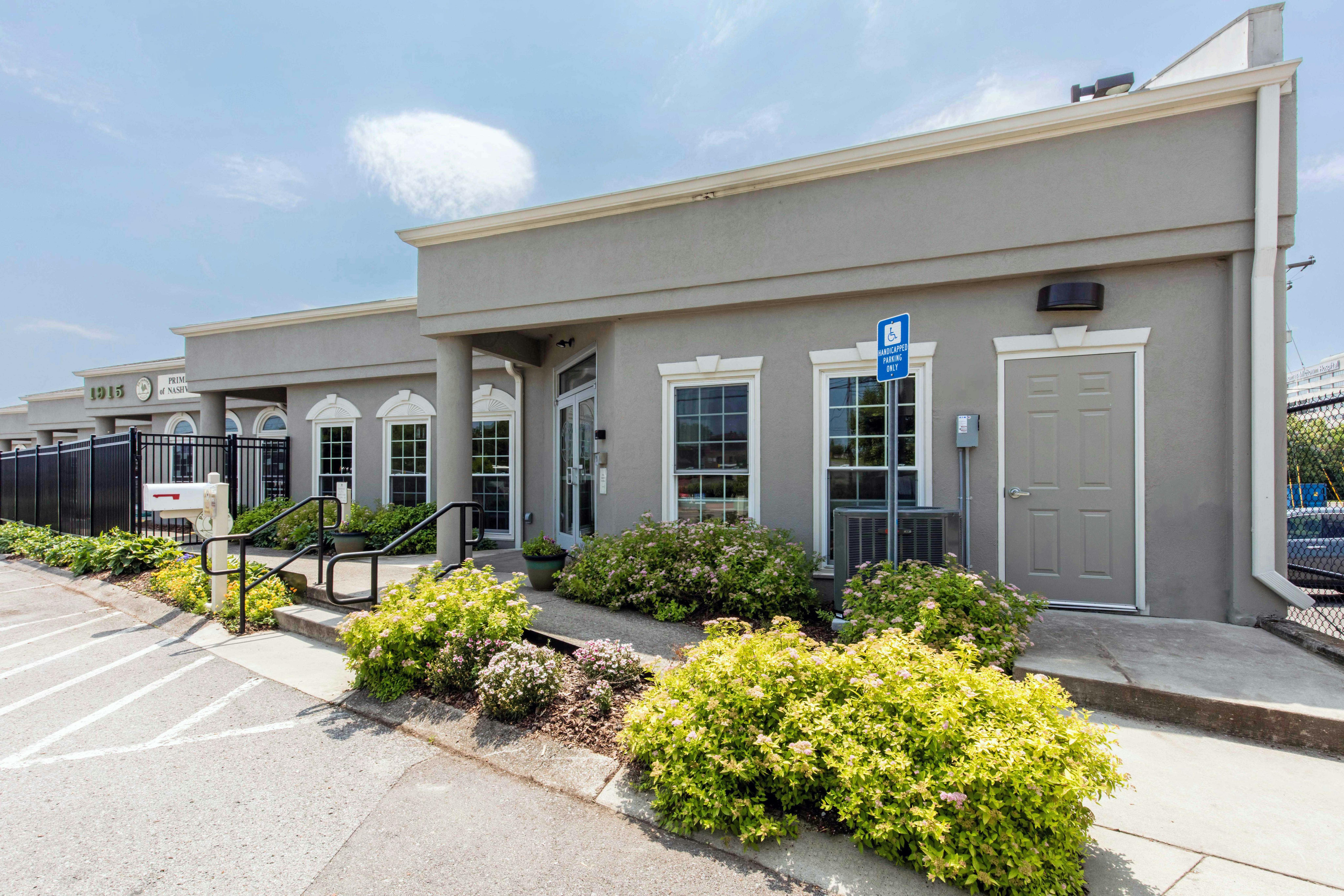 Exterior of a gray building with multiple windows, a door, and landscaping