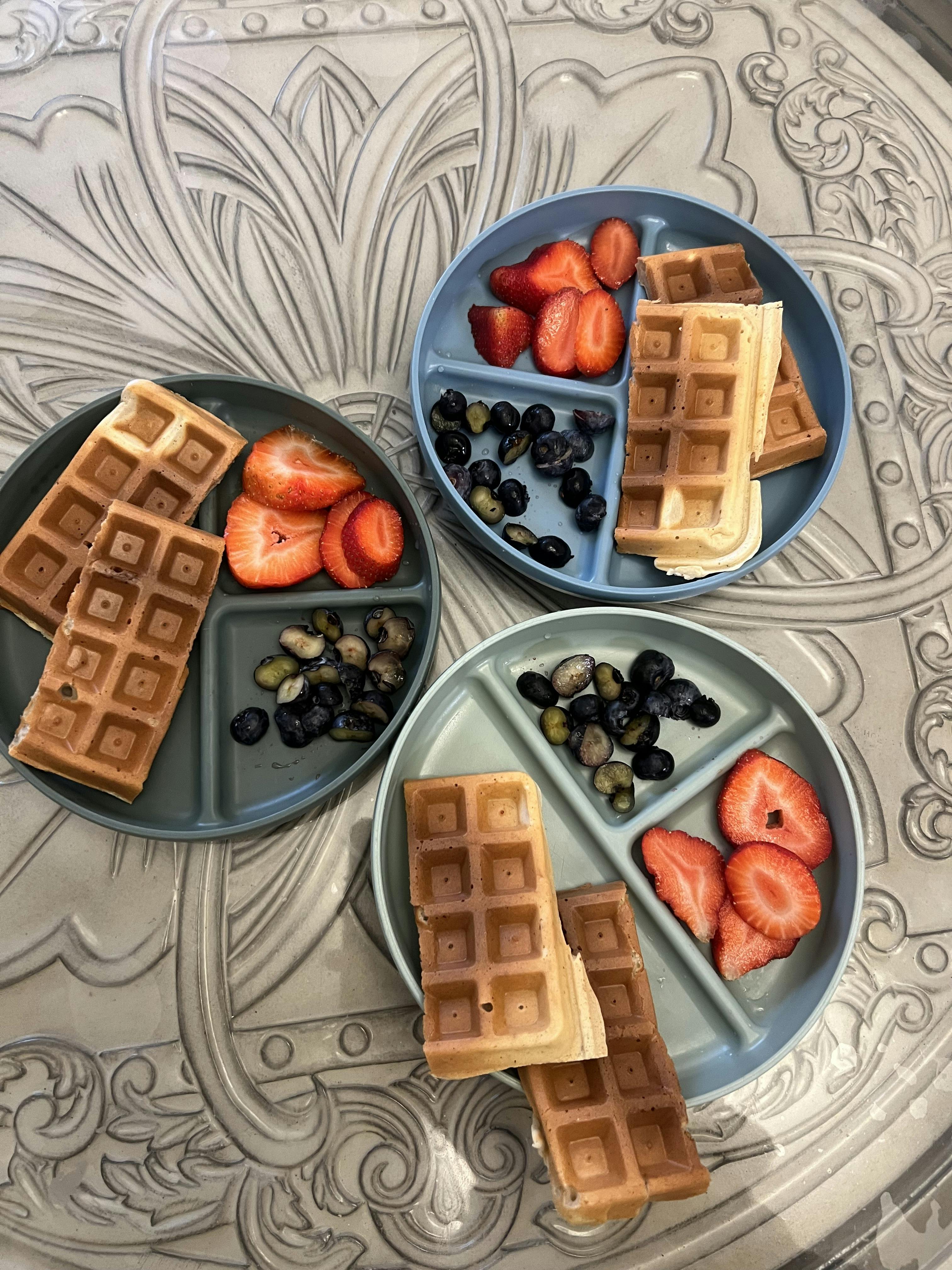 Three sectional plates with waffles, sliced strawberries, and blueberries