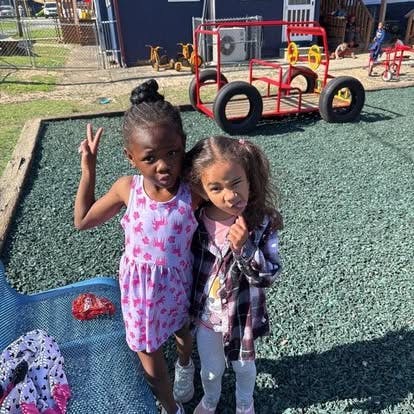 Two children standing on a playground, one making a peace sign
