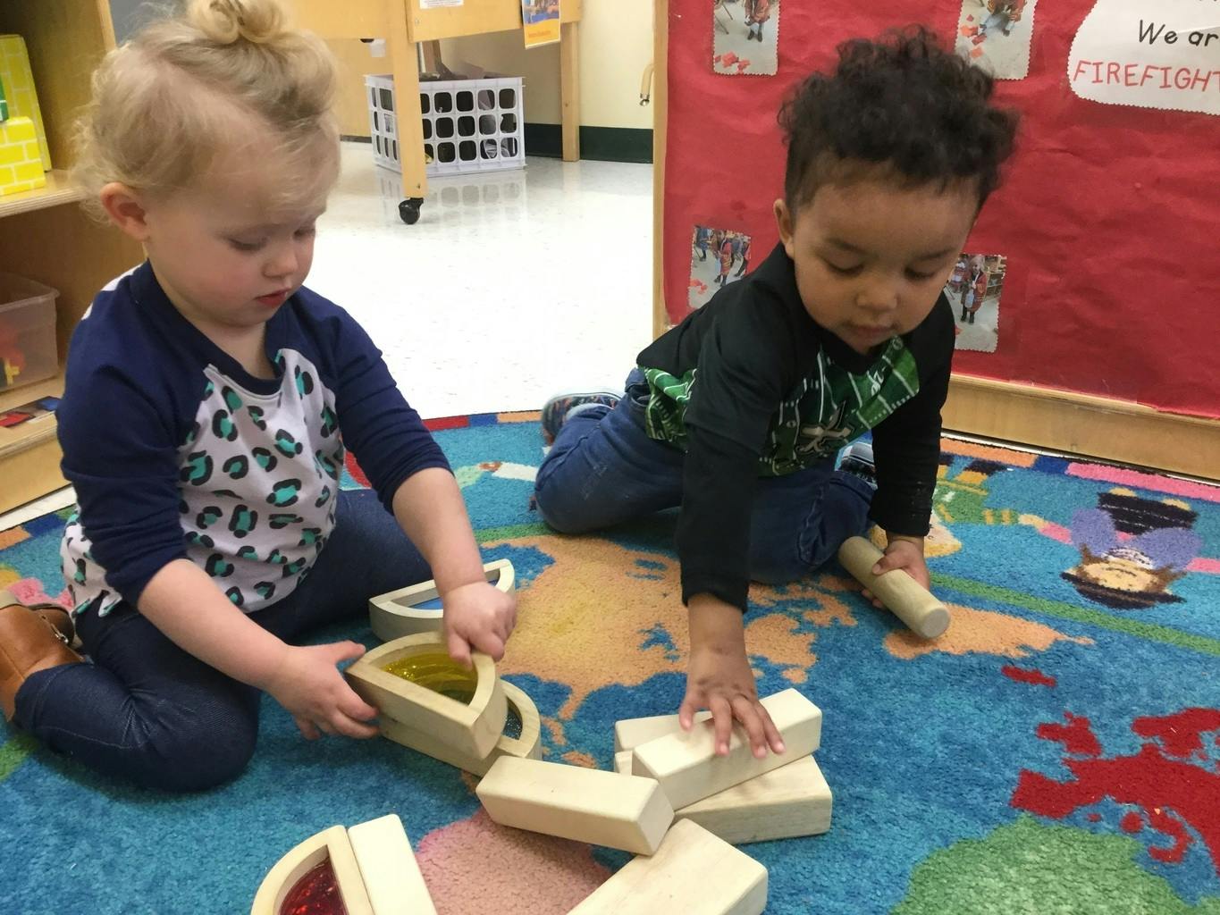Two children playing with wooden blocks on a rug