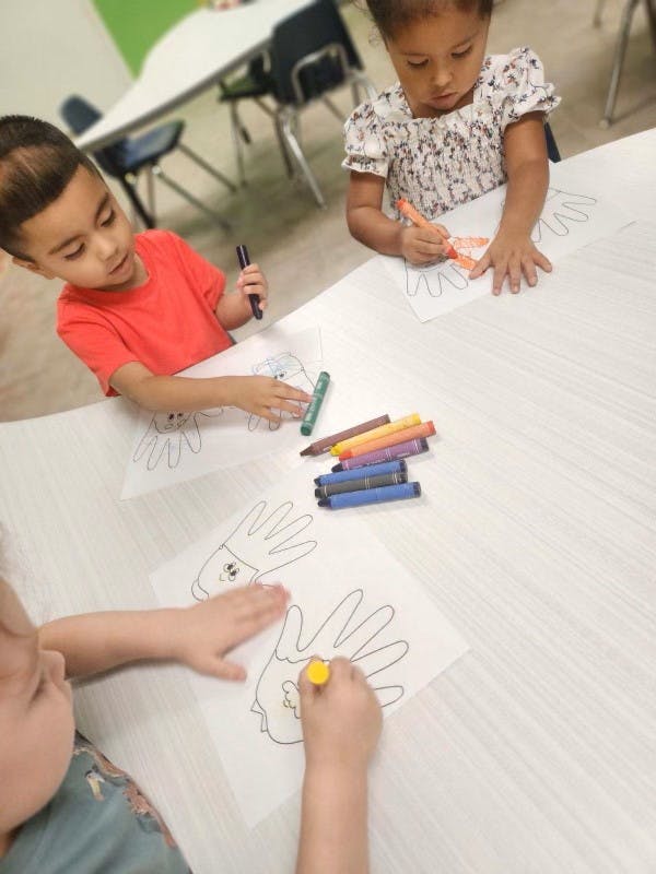 Children coloring handprint outlines on paper atable