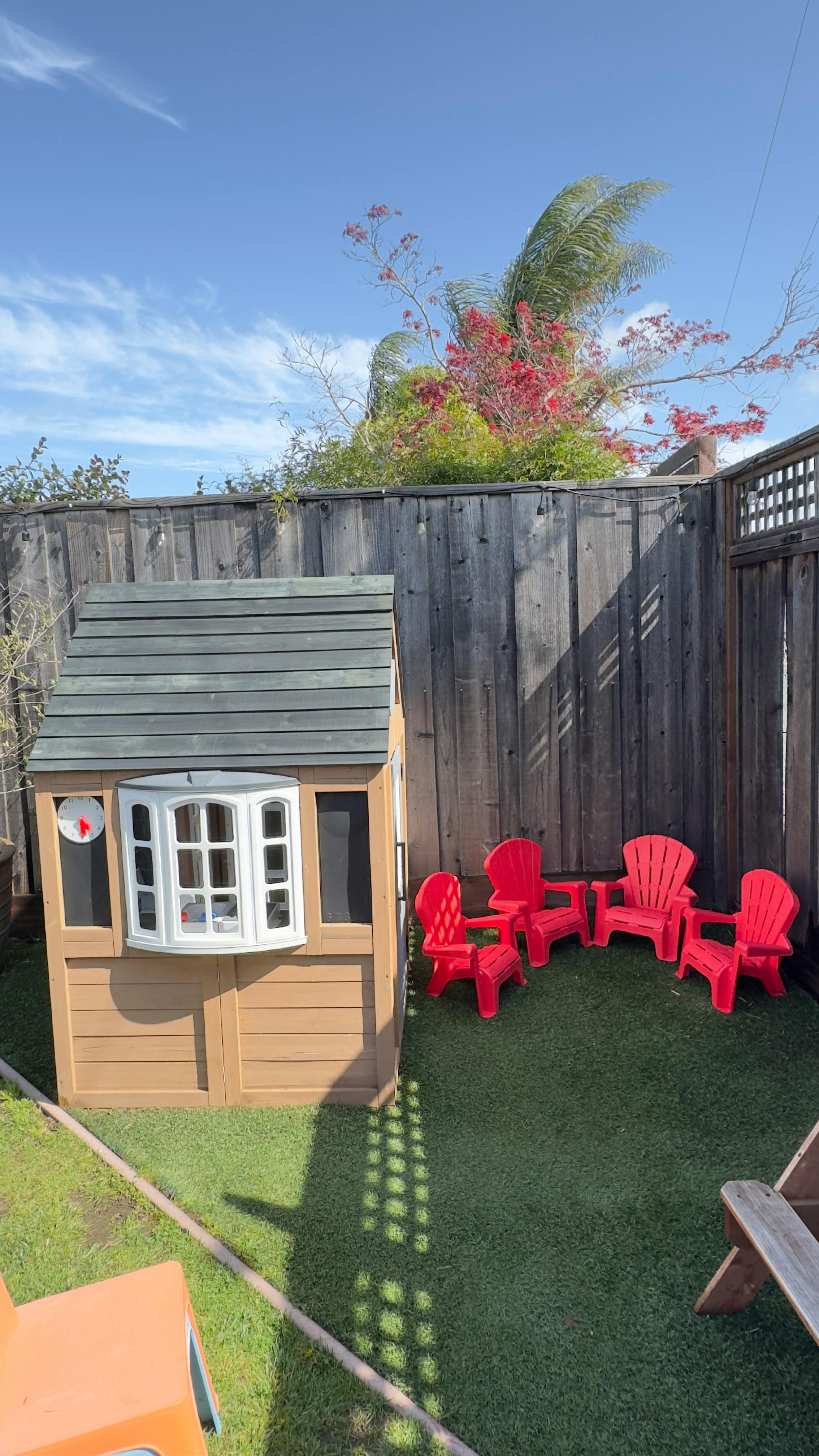 Playhouse and red chairs on artificial grass in a fenced yard
