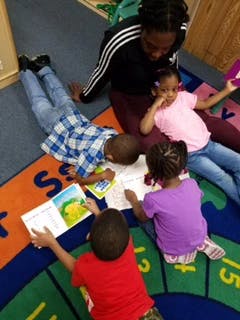 Adult and three children reading books on a rug