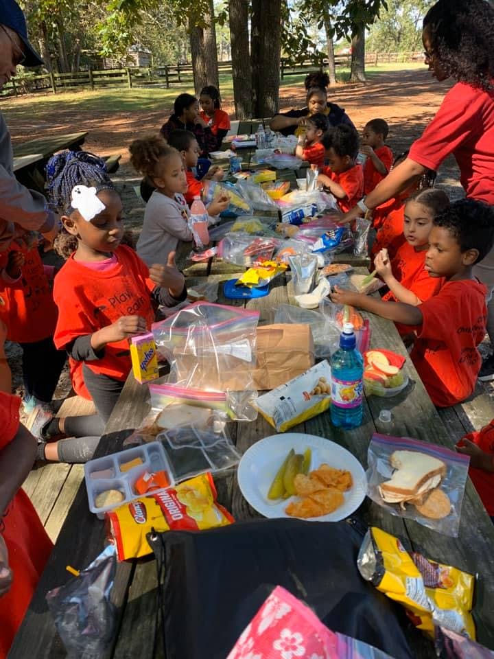 Children and adults eating lunch at a picnic table outdoors