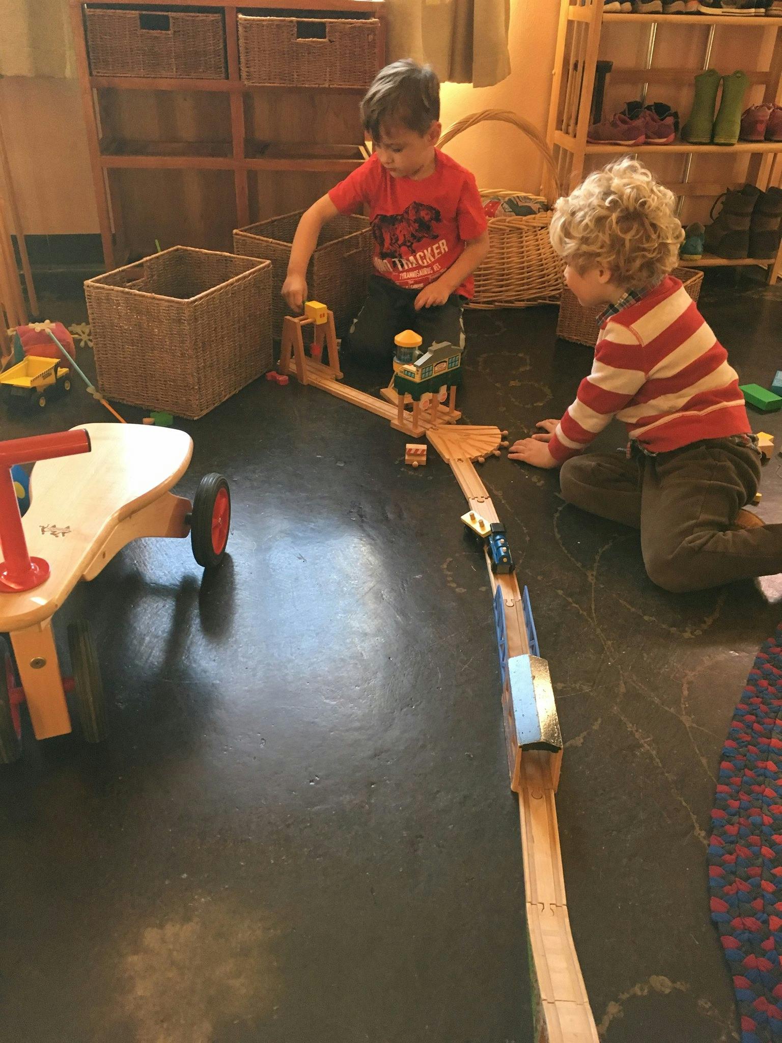 Two children playing with a wooden train set on the floor