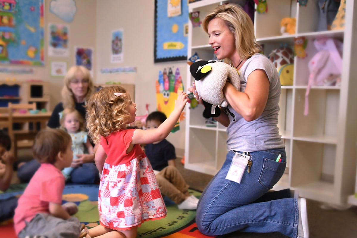 Adult kneeling with a puppet interacting with a child in a classroom