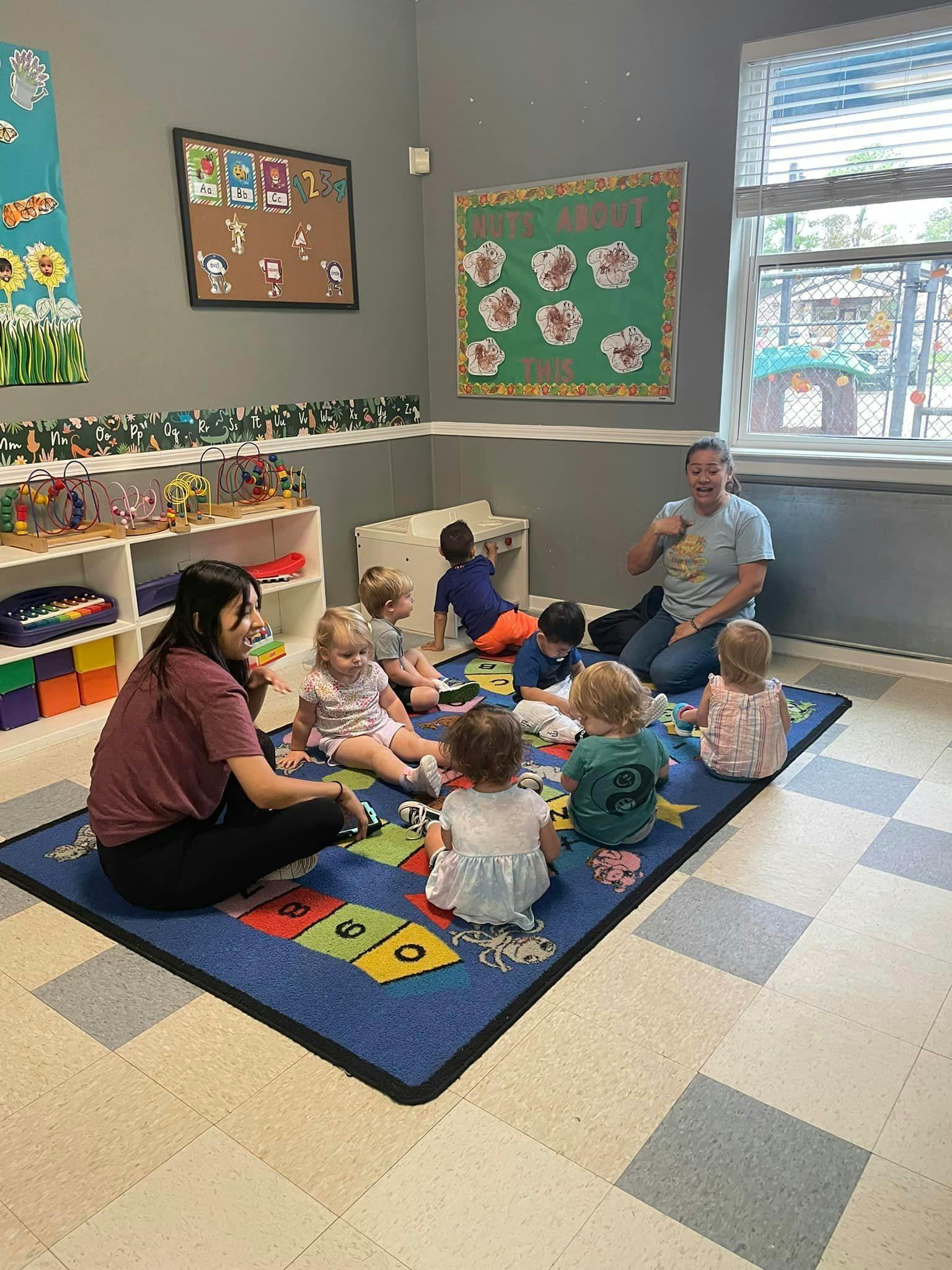 Two adults and multiple children sitting on a rug in a classroom