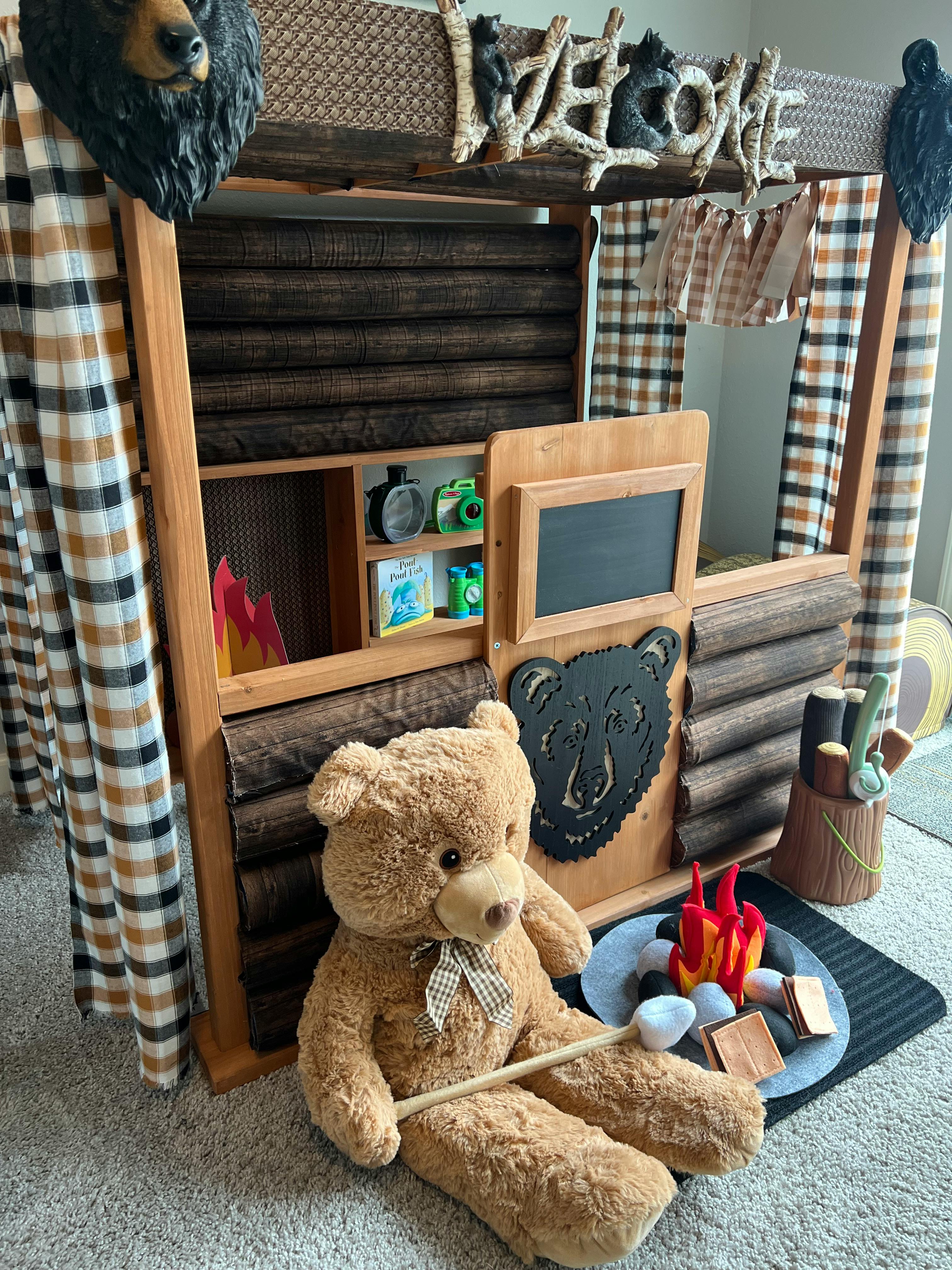 Bear-themed wooden playhouse with a large teddy bear and toy campfire