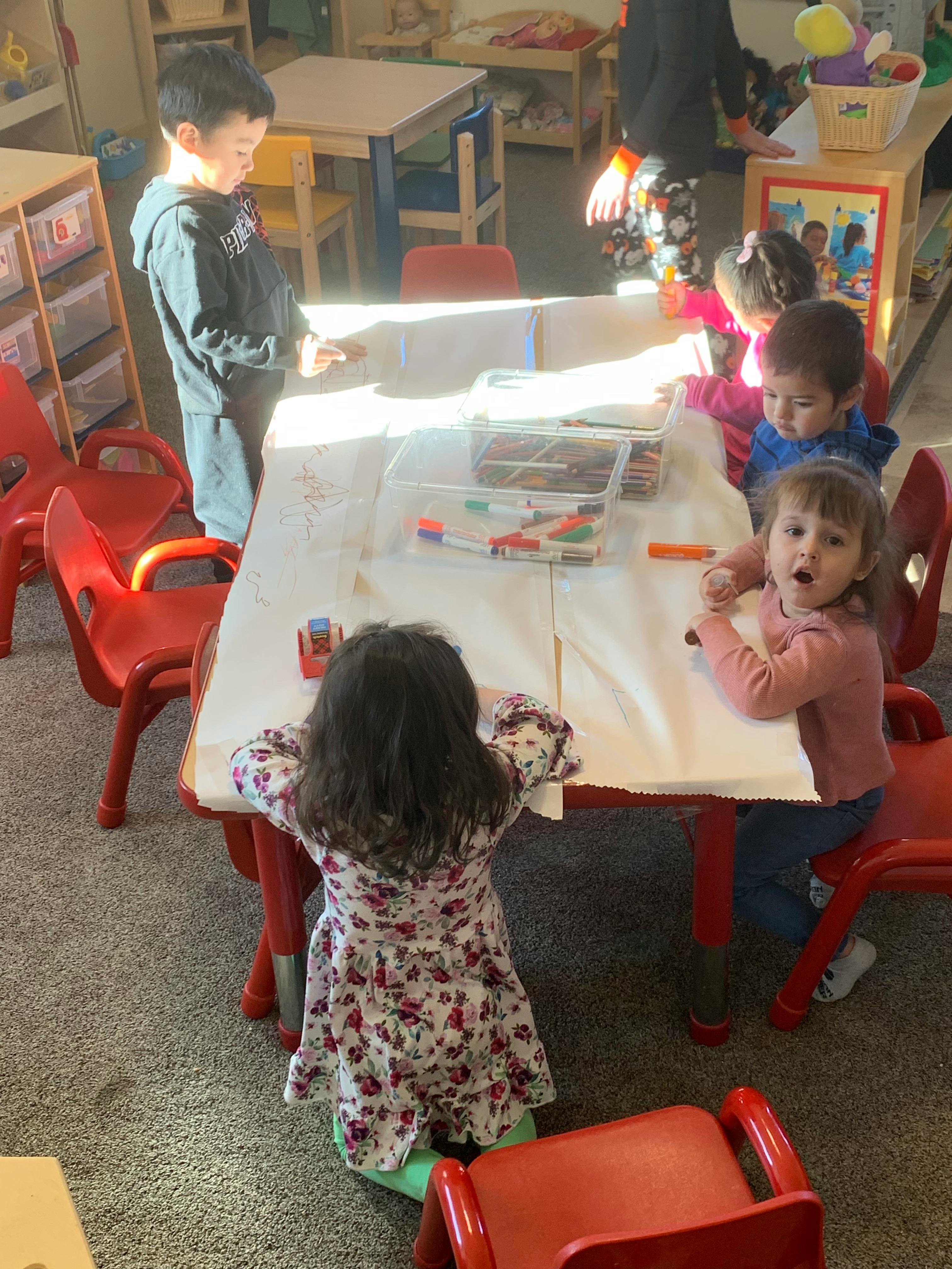 Children sitting at a table drawing with markers
