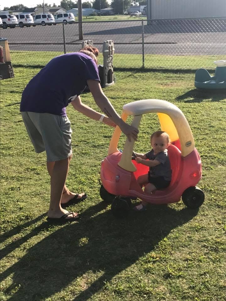 Person pushing a child in a toy car on grass