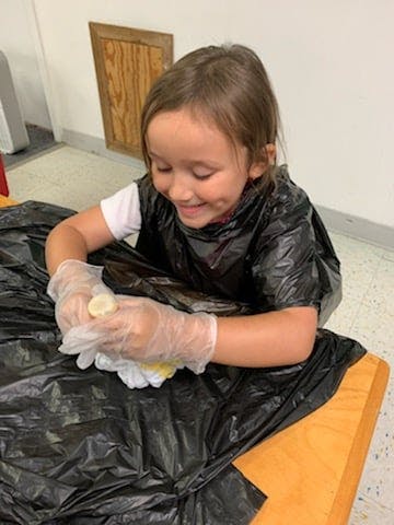Child wearing gloves and black smock working with hands