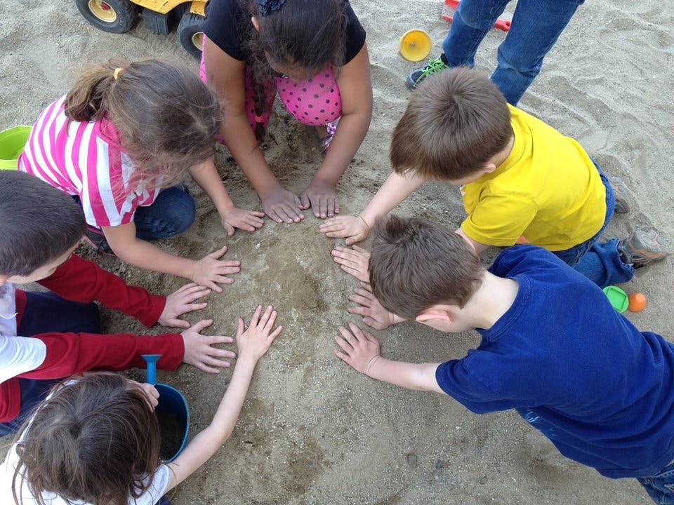 Children playing in sand, hands forming a circle