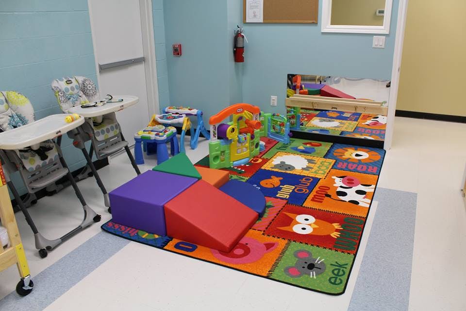 Playroom with colorful rug, soft play blocks, and high chairs