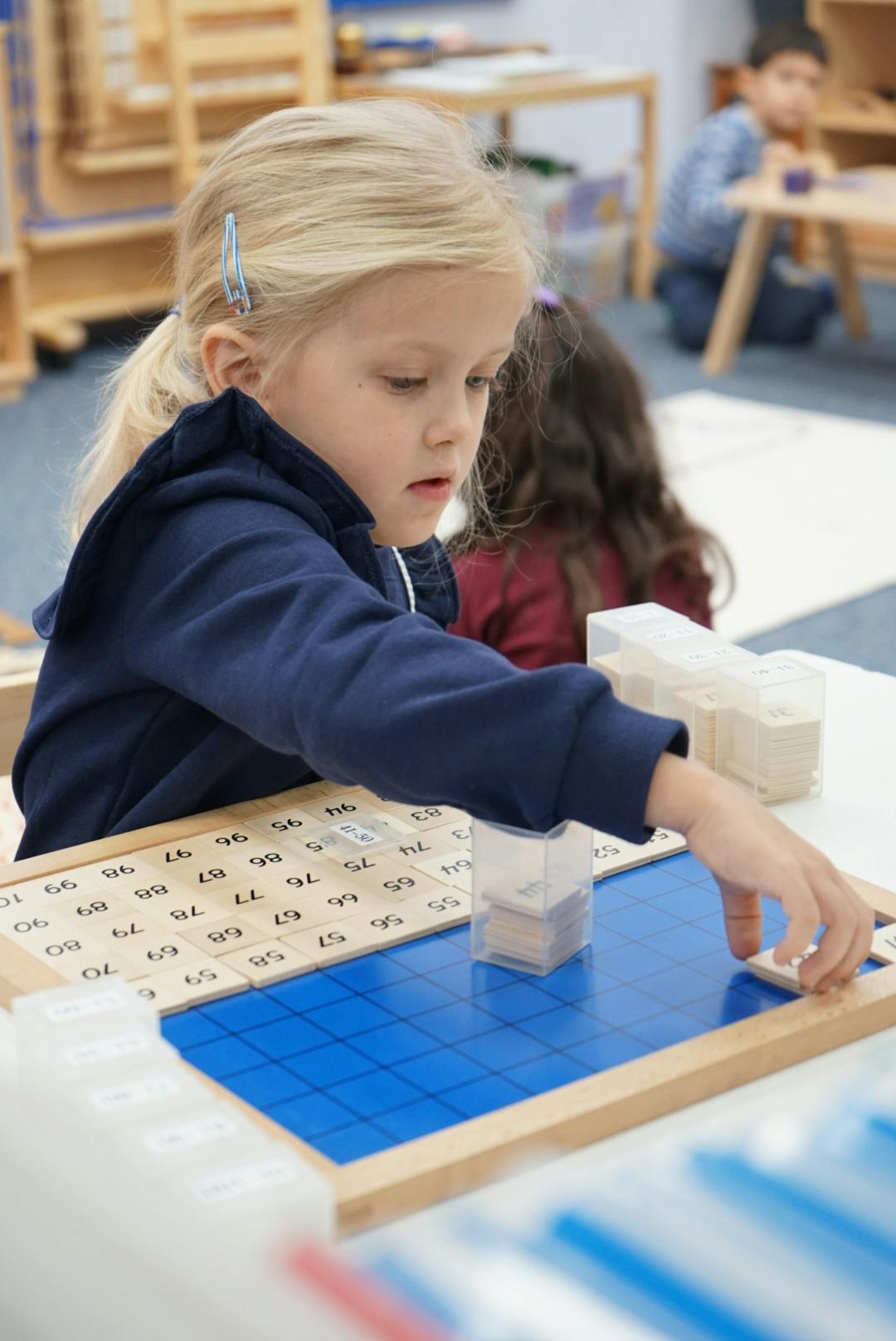 Child working with a number board and blue grid insets in a classroom