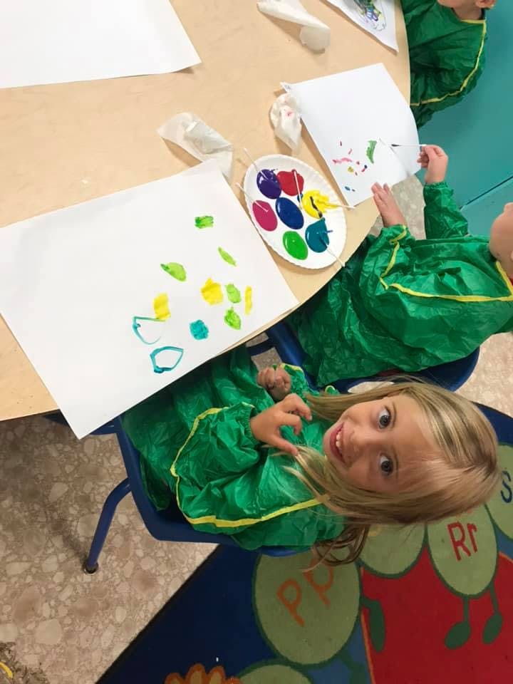 Child in green smock painting at a table