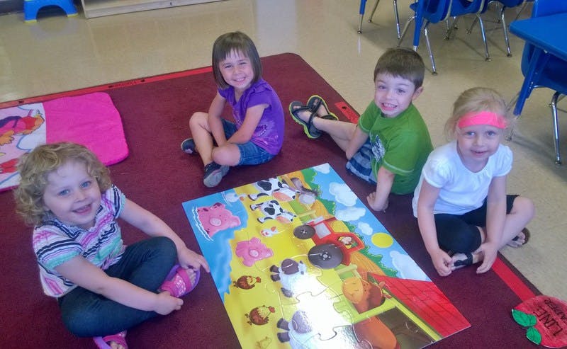 Four children sitting on a rug with a colorful puzzle