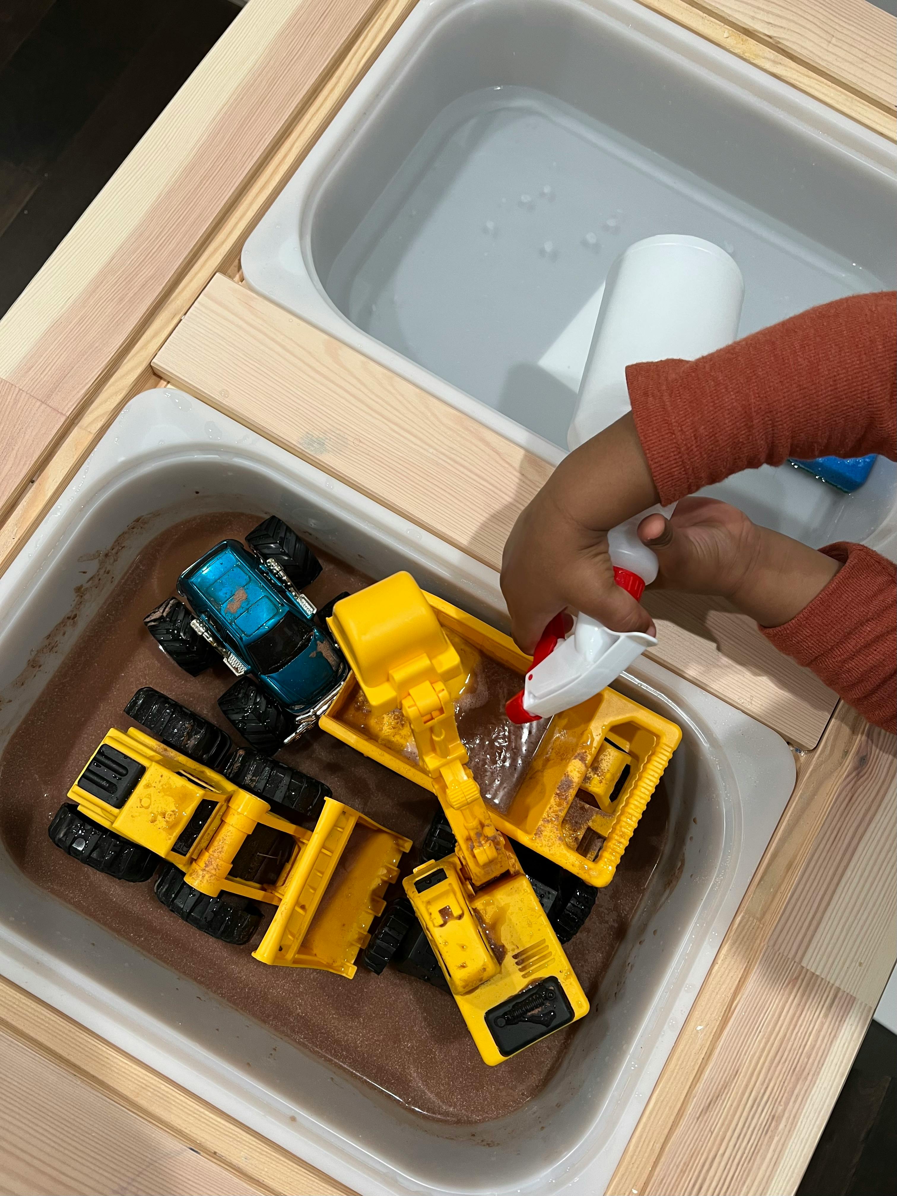 Child playing with toy trucks in a water table