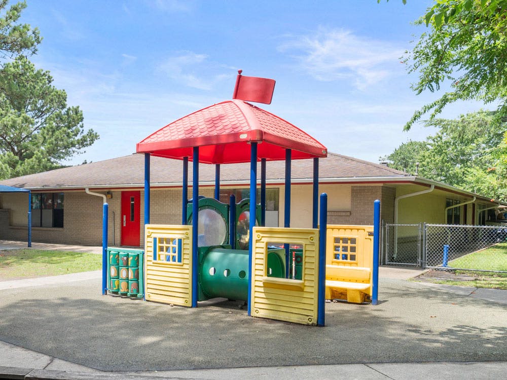 Colorful playground structure with red roof and yellow panels, on a soft surface