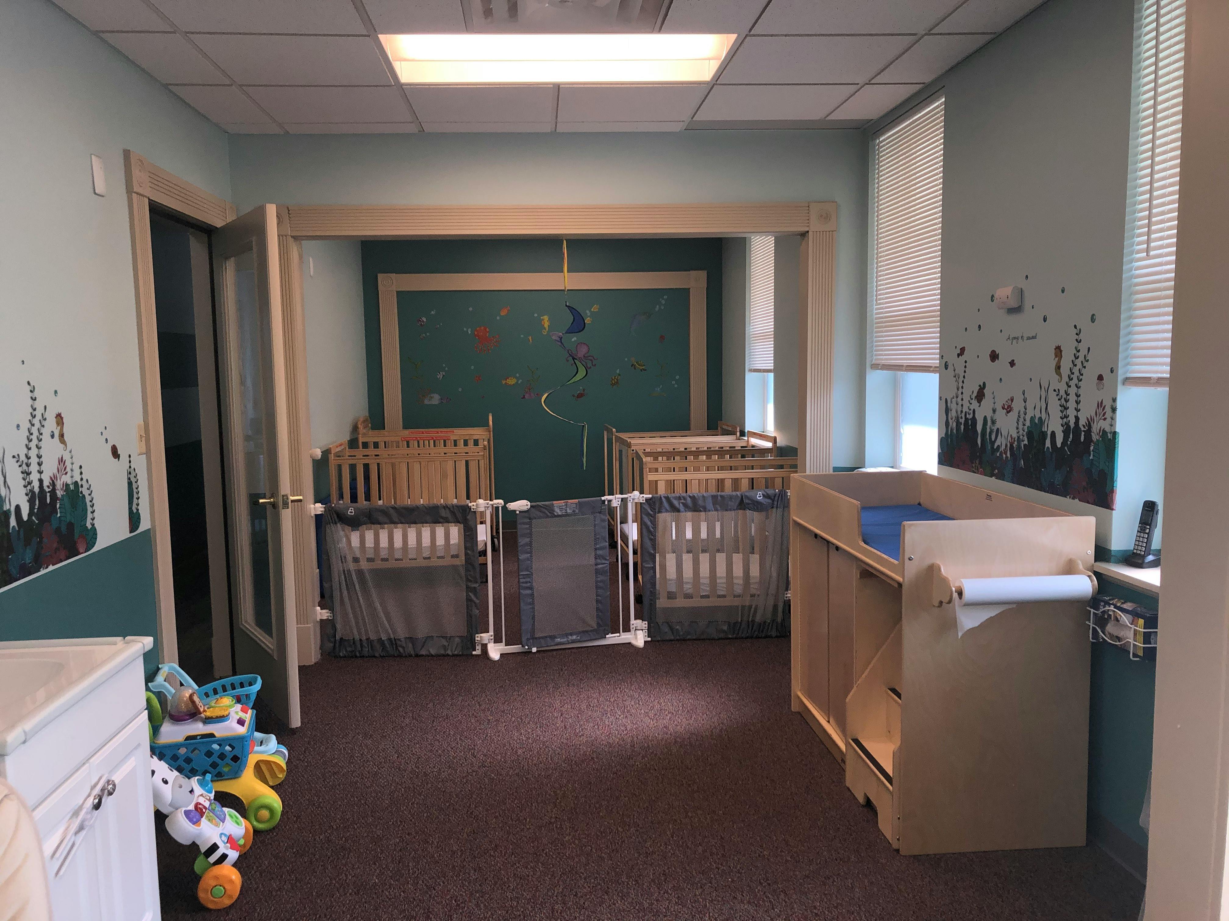 Room with multiple cribs, baby gates, and a changing table