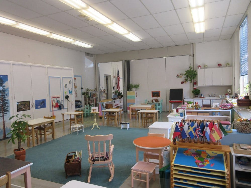 Classroom with small tables and chairs, a rocking chair, and flags