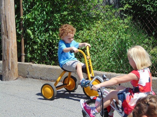 Child on a tricycle next to another child on a bike