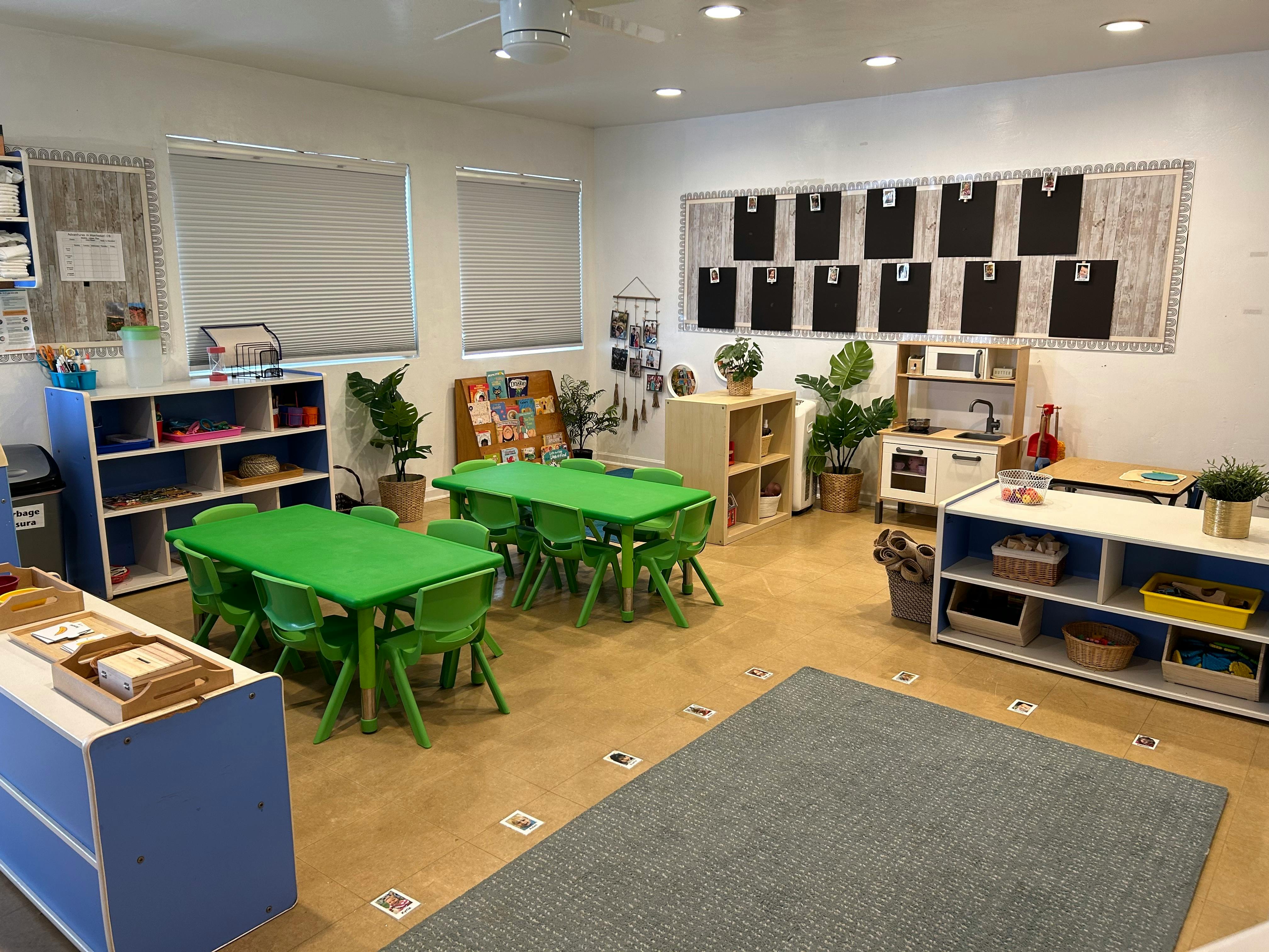 Classroom with green tables and chairs, shelves, and a rug