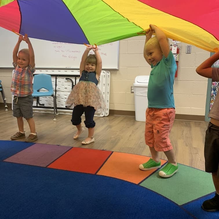 Children holding up a colorful parachute in a classroom