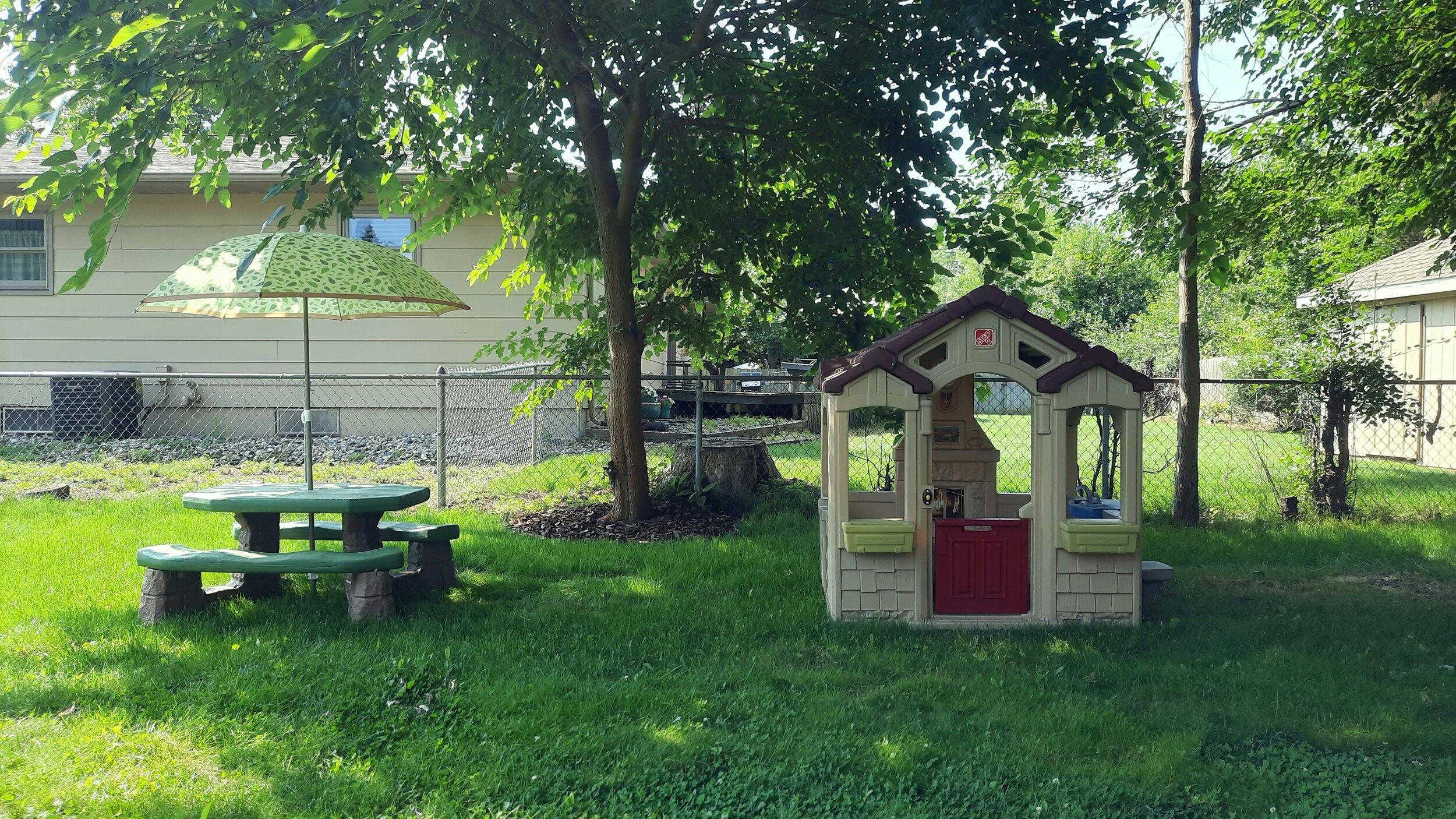Picnic table with umbrella and playhouse in a grassy yard