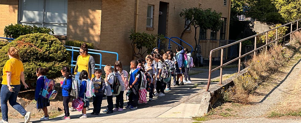 Adults and children with backpacks lining up outdoors