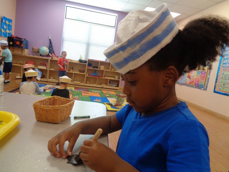 Child in a hat working on a craft at a table in a classroom