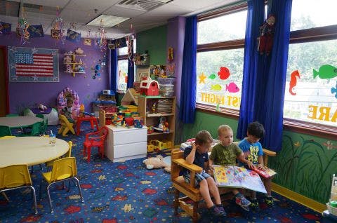 Three children sitting on a bench reading a book in a classroom