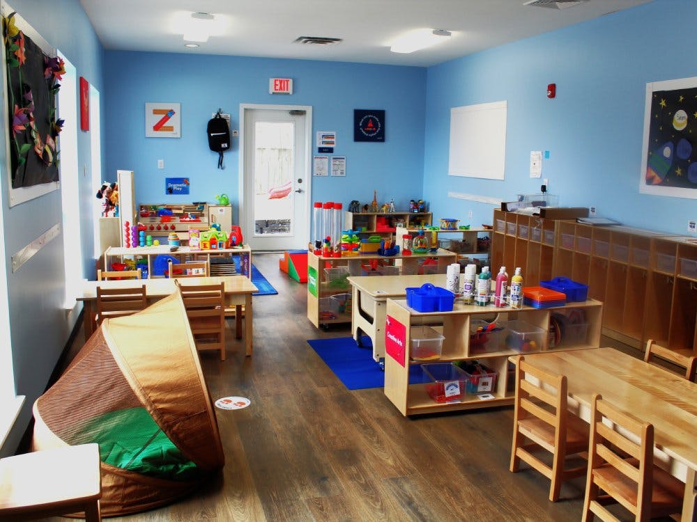 A classroom with tables, chairs, shelving units filled with toys, and a play tent