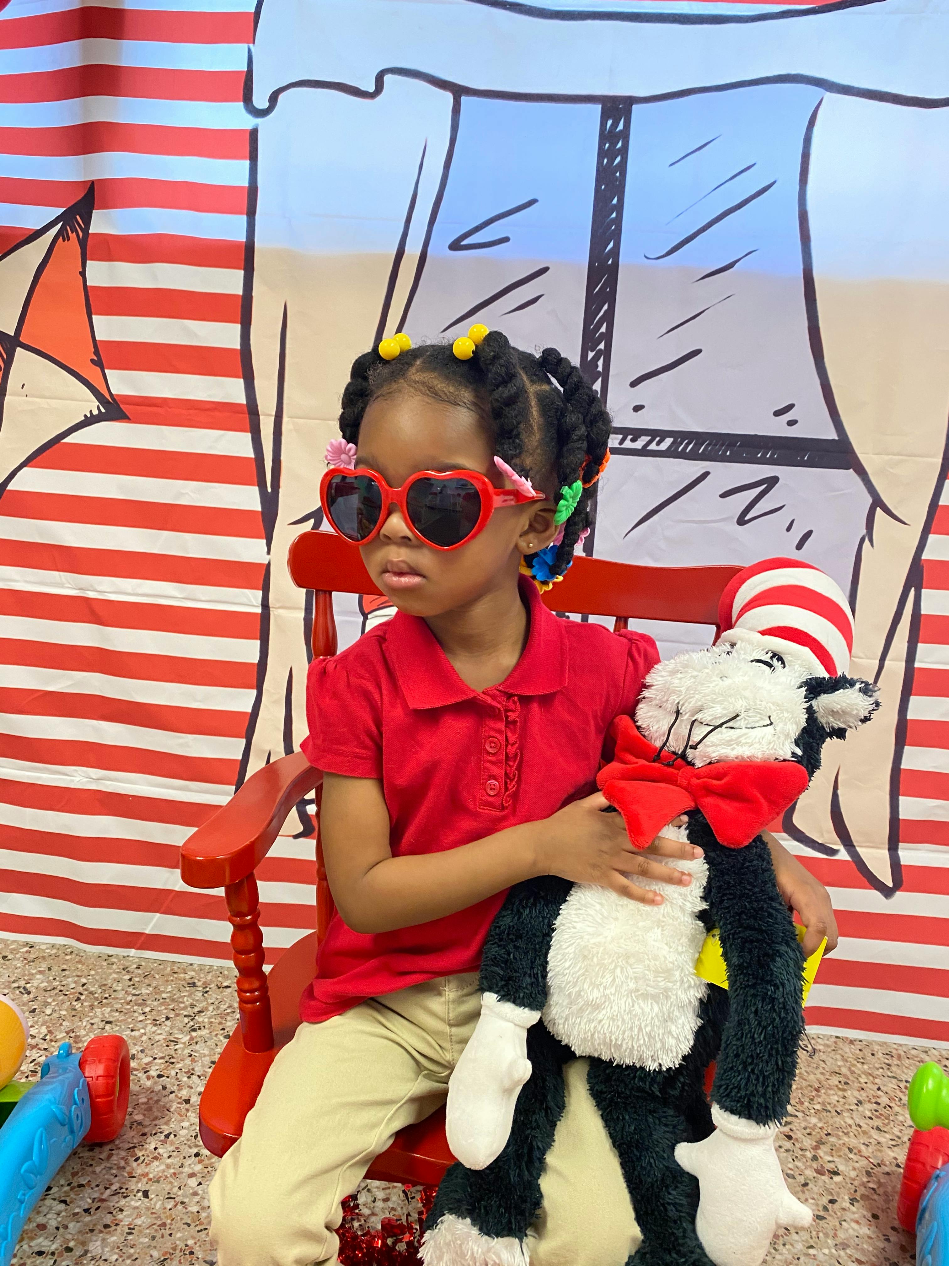 Child in heart sunglasses holding a stuffed animal